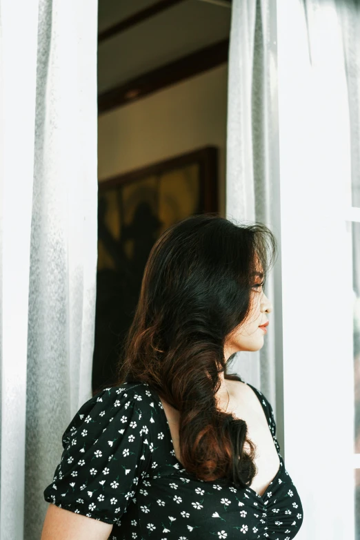 woman looking out a window with white curtains