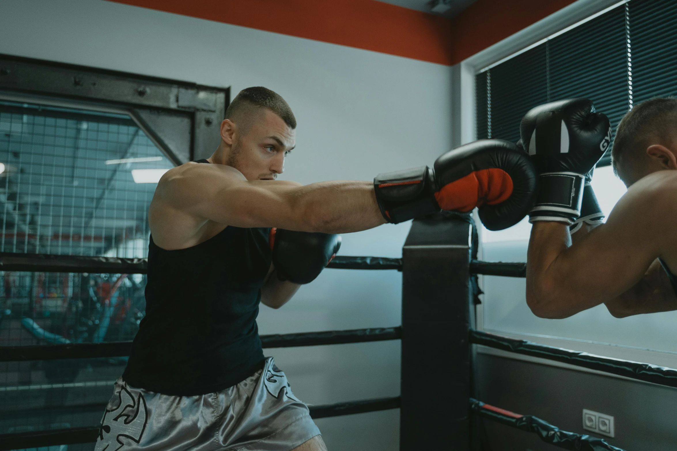 two men engaged in boxing, one in boxing gloves is holding his elbow up as the other waits