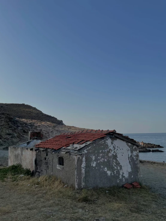 a building with a roof is standing on a field by the ocean