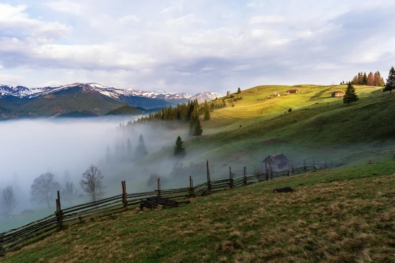 a hilly hillside with fence and snow capped mountains