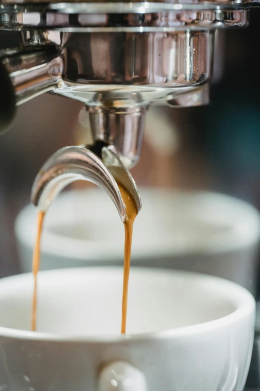 coffee pours from a coffee machine into a white cup