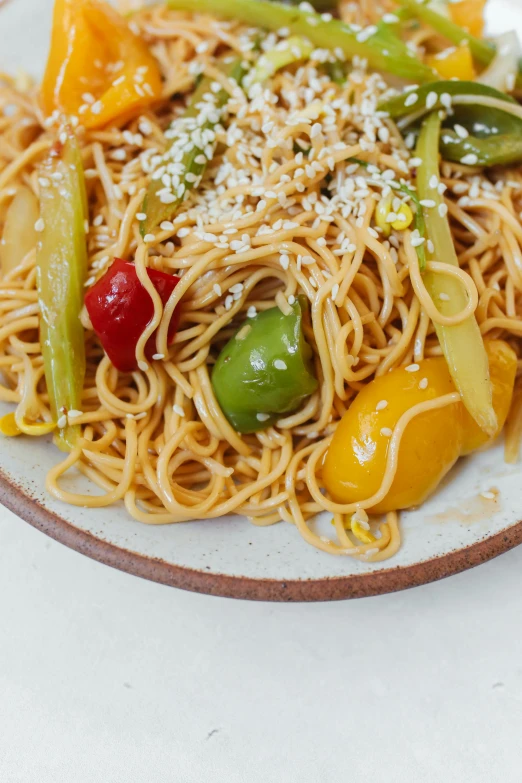 the plate has noodles, bell peppers and sesame seeds