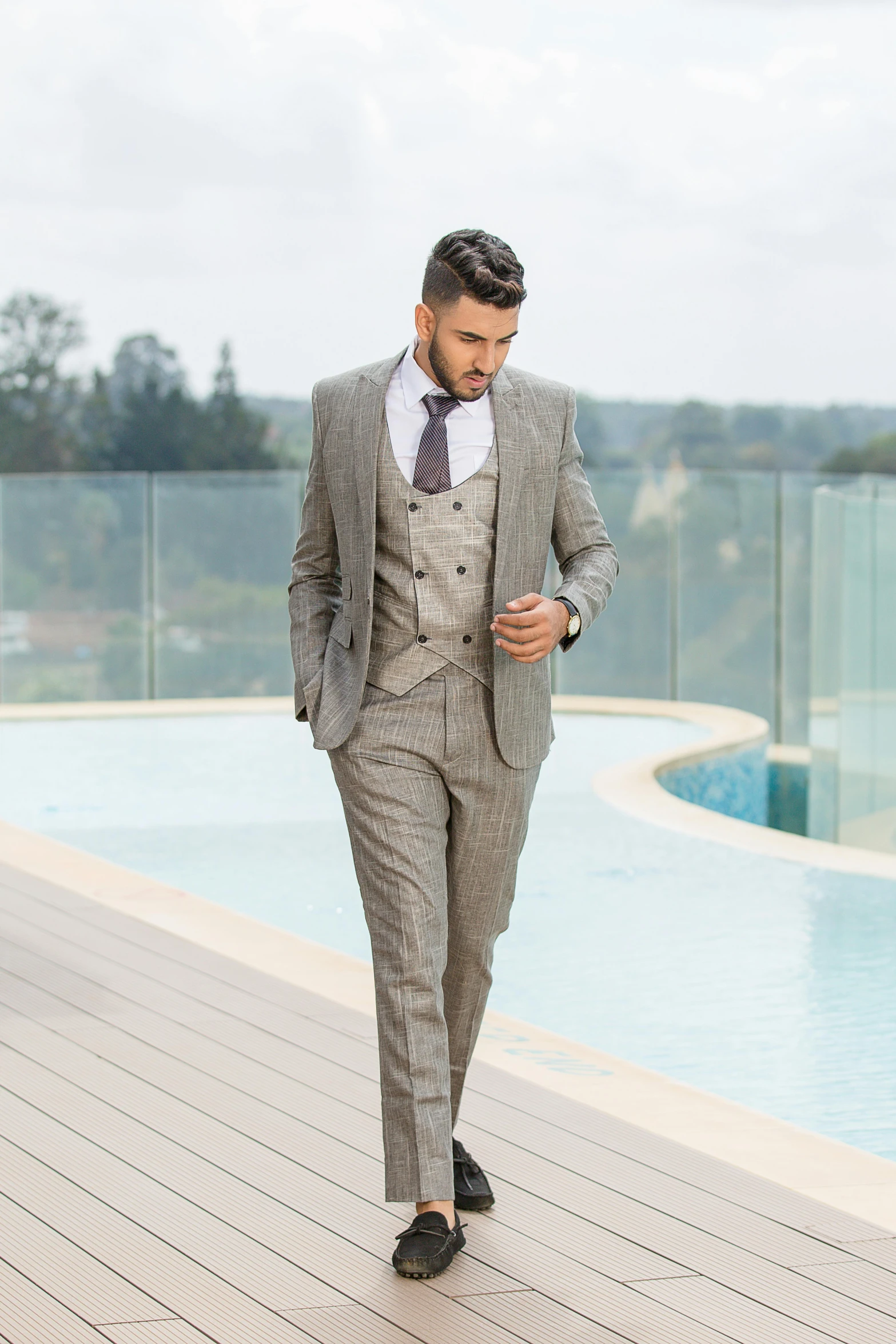 a man in a gray suit walking past a swimming pool