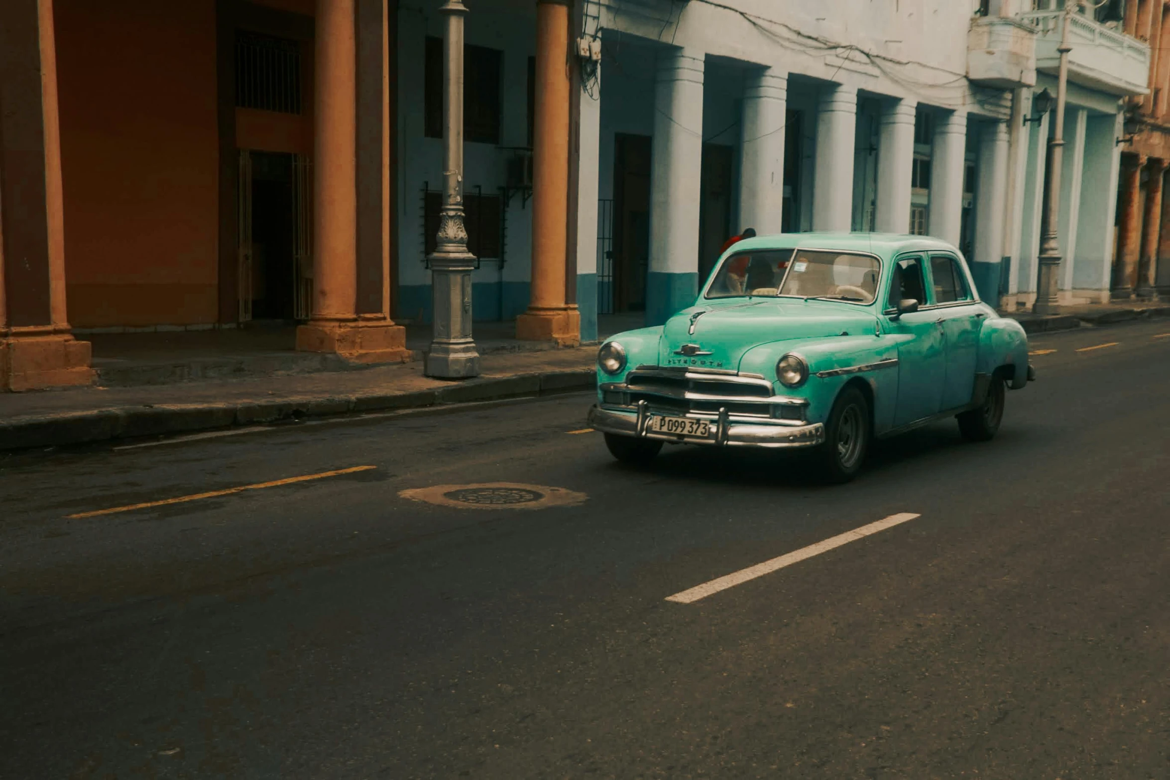 a green classic car drives down the road in front of old buildings