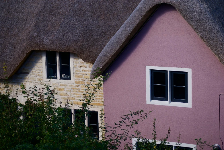 a pink thatch roofed house with two windows