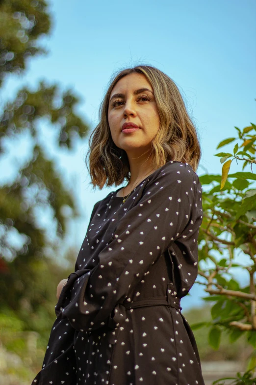 a woman in polka dot print dress posing near a tree