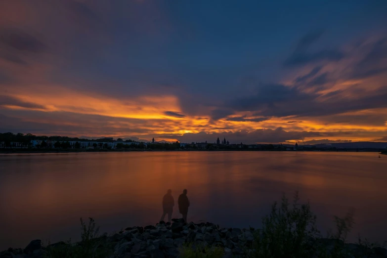 two people standing near the water watching the sun rise