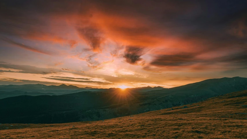 a hill that has a mountain in the distance with a cloudy sky