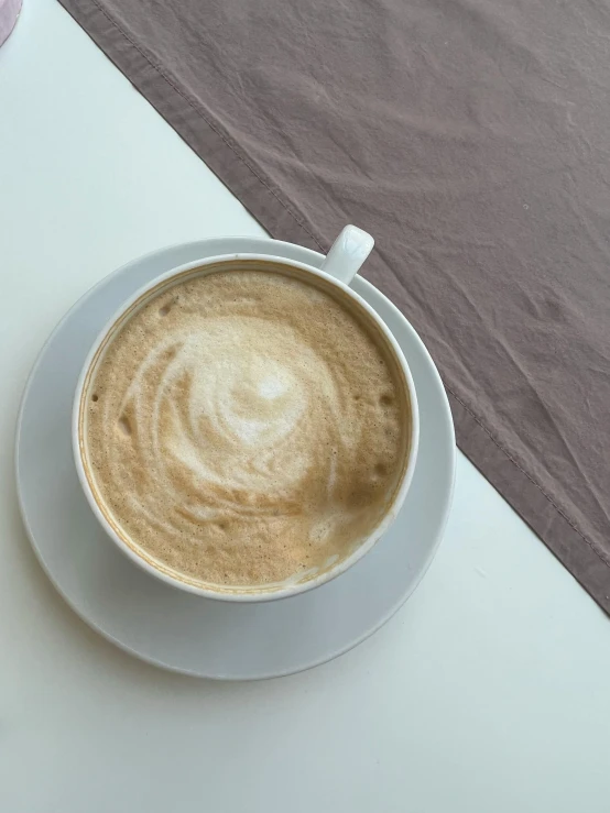 a cappuccino with a white saucer and spoon on a white surface