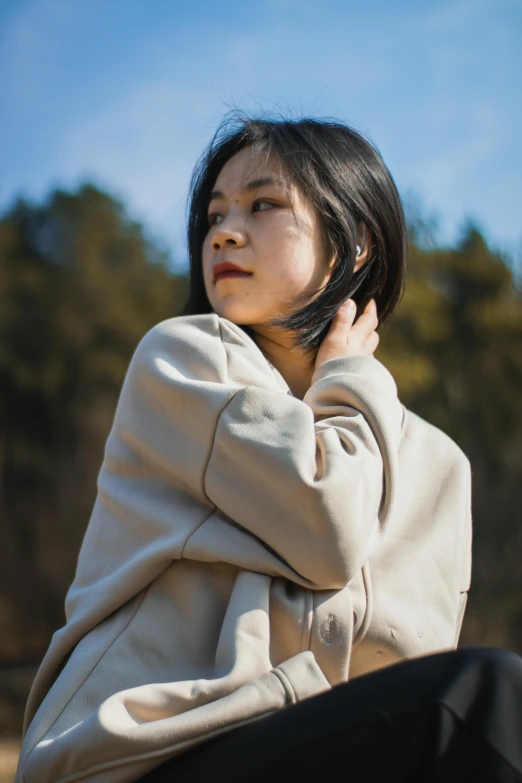 a  sitting in front of trees wearing a sweater