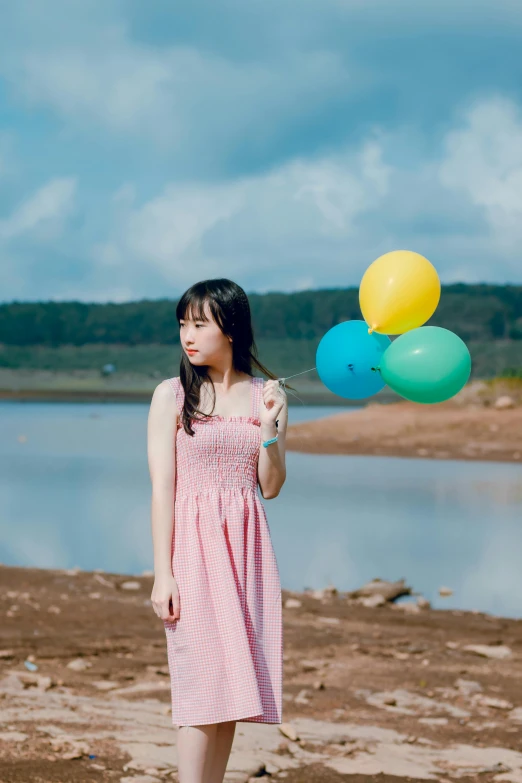 a young lady is holding some balloons on a beach