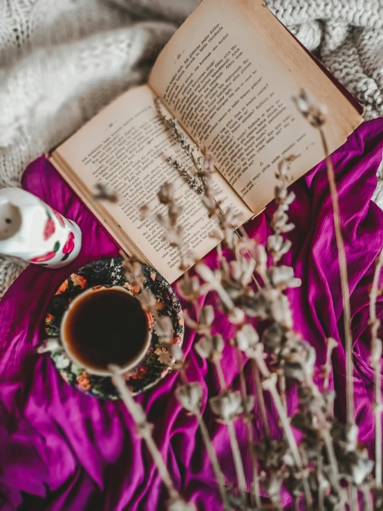 an open book on a table next to flowers and a cup of coffee