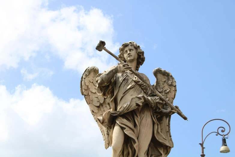 an angel statue with a stick against a blue sky