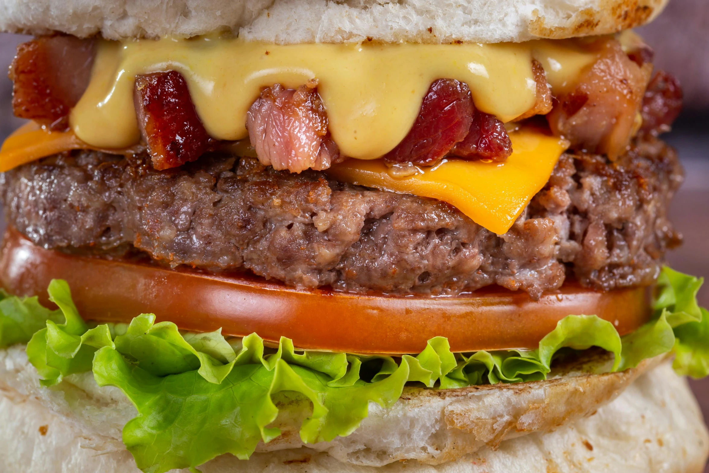 the large hamburger is decorated with bacon, cheese, lettuce, and tomatoes