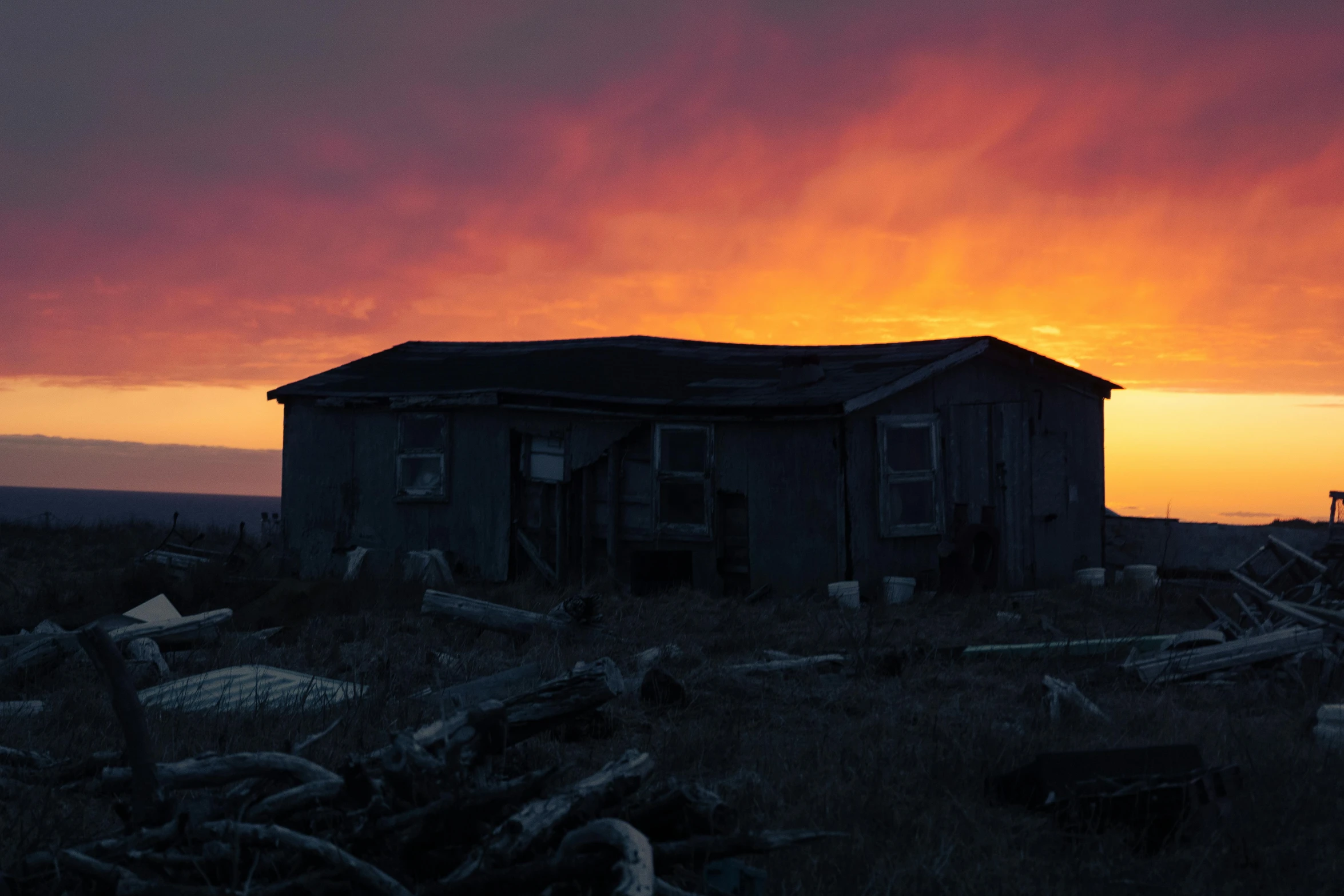 a dark house sits in an open field as the sun sets