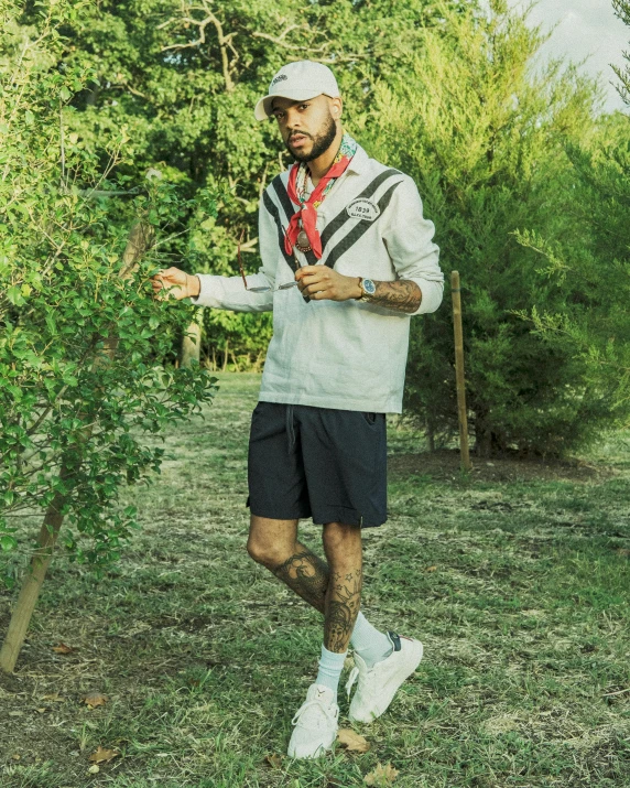 a man with a hat, sweater and shorts standing in a field