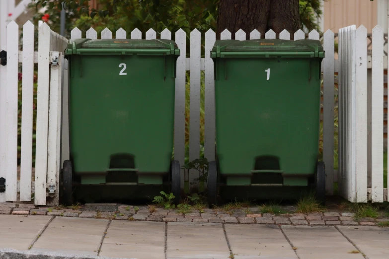 a couple of trash cans sit outside in front of a fence