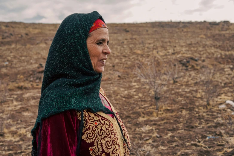 a woman with green and red head scarf standing in the middle of a dry field