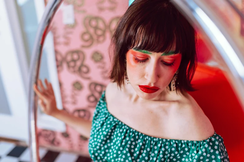 a young woman with green eye makeup and matching lip color poses in a mirror