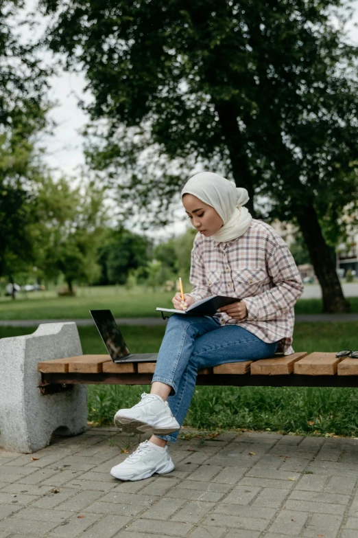 a woman sitting on a bench reading and using a laptop