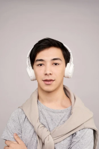 a young man wearing headphones and standing in front of a gray background
