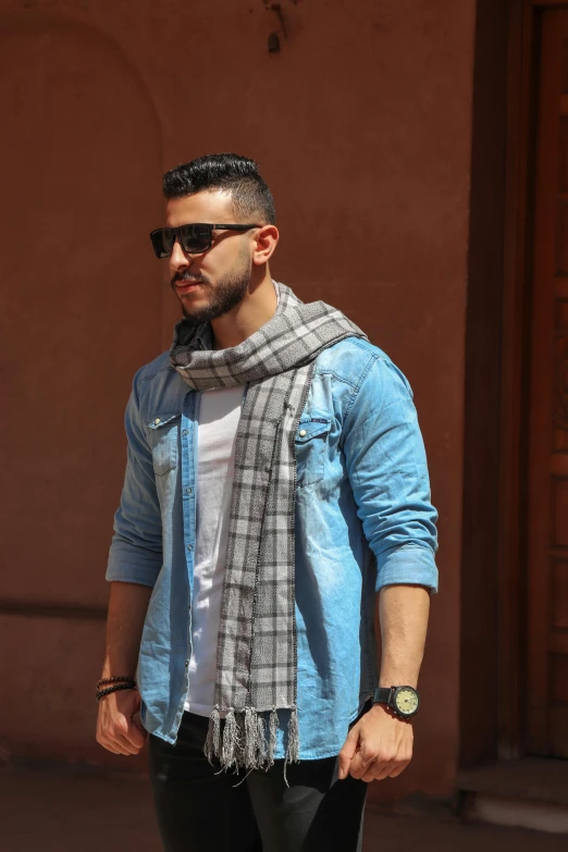 a man with sunglasses and a scarf is standing on a sidewalk
