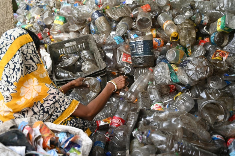 a person sits in front of an overflowed pile of plastic bottles