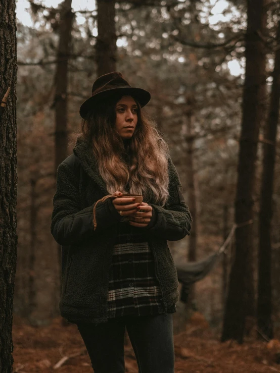 the woman stands near some trees and looks at her cell phone