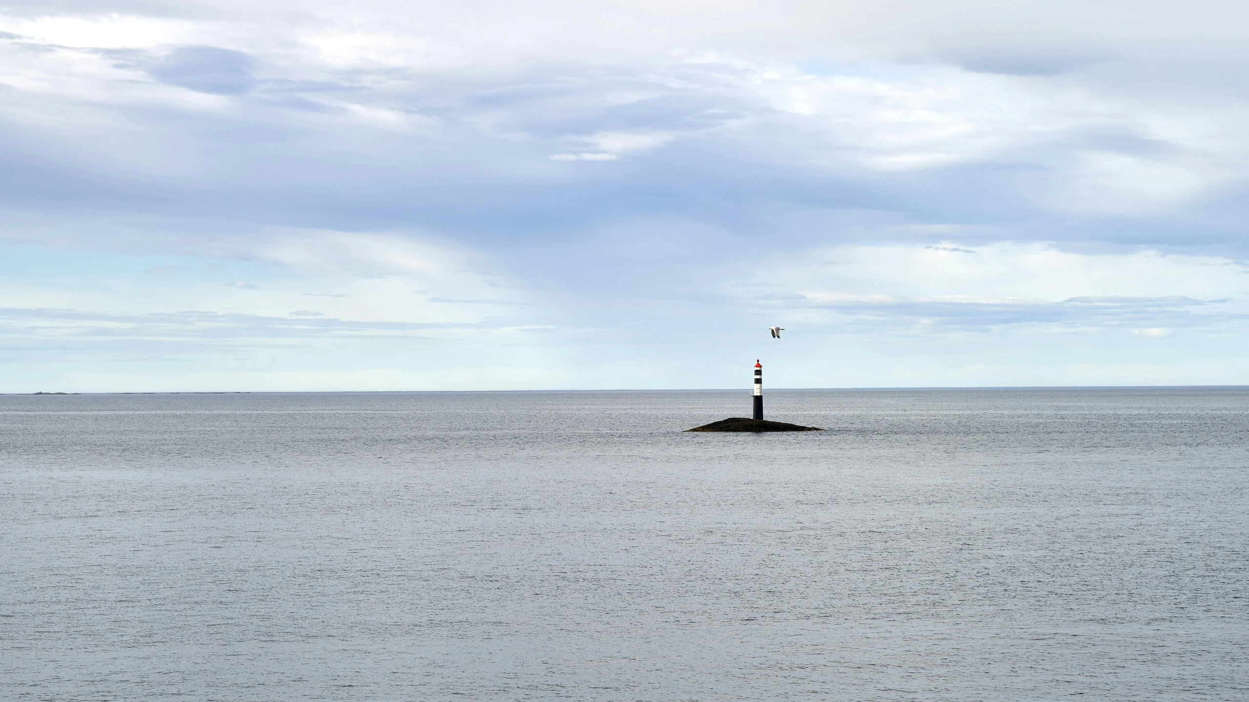 a lone lighthouse out in the ocean under a cloudy sky