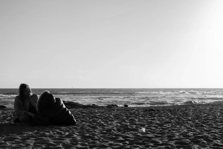 two women sitting on the sand at a beach