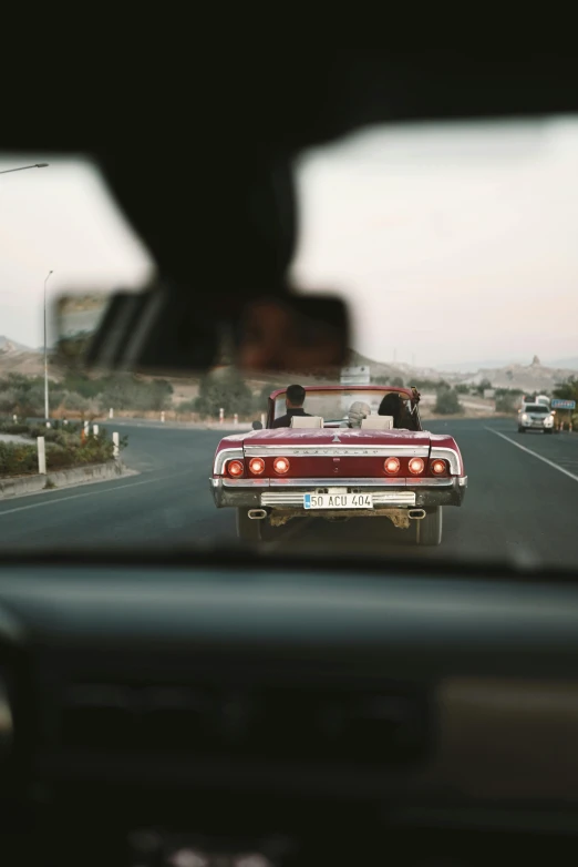 view from the front seat of a car of the front end of a red pickup truck driving on a street