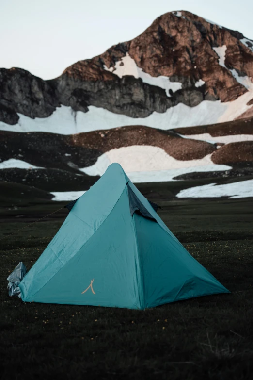 a camping tent sits on the ground beneath a mountain