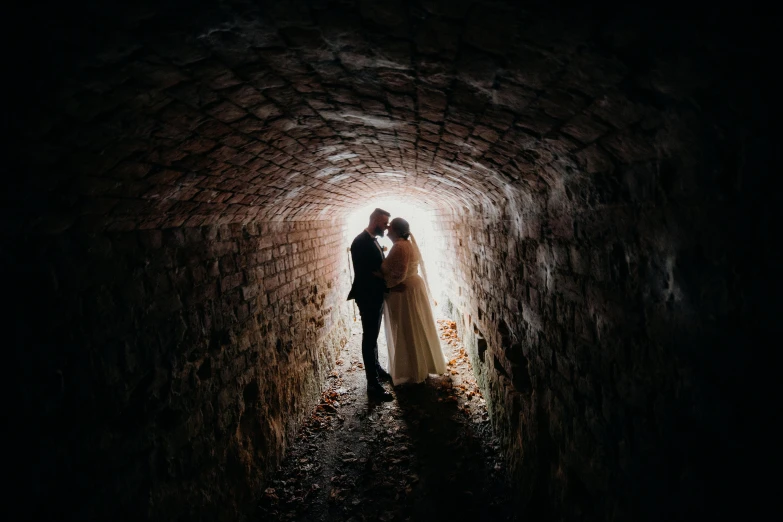 a couple standing in a tunnel with their wedding gown on