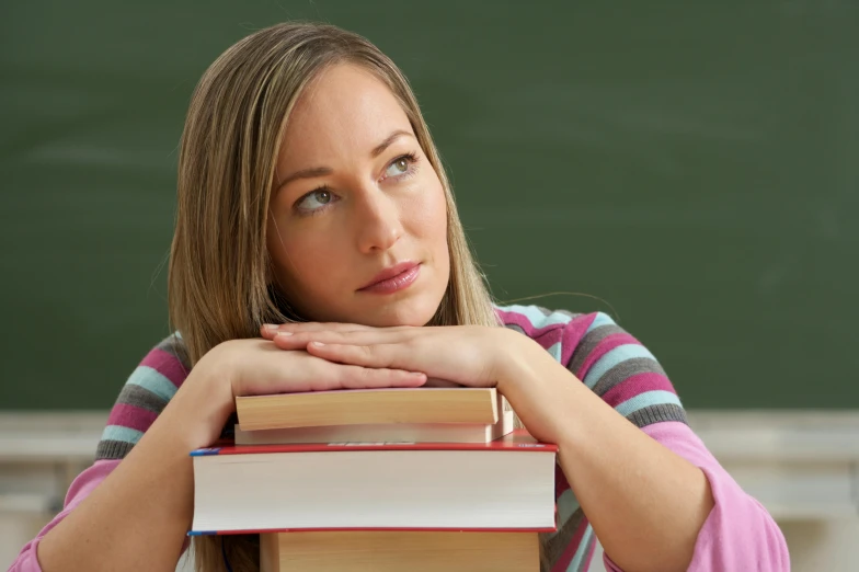 the young lady with a stack of books is looking at the camera