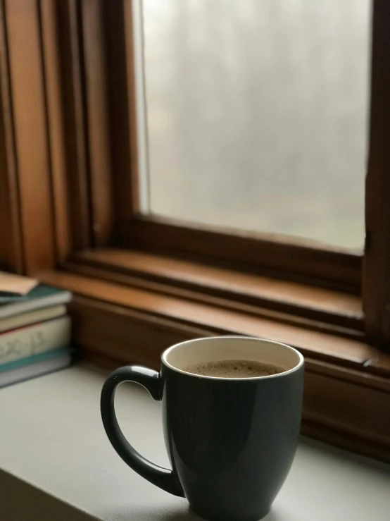 a cup sitting on top of a window sill next to some books