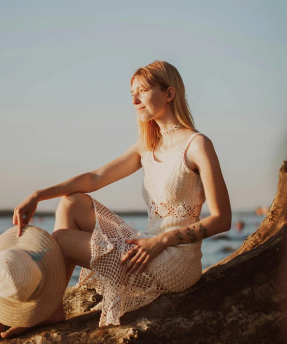 a woman with a hat sitting on a rock by the ocean