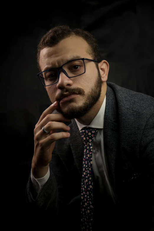 a man in suit and tie standing with his finger under his chin