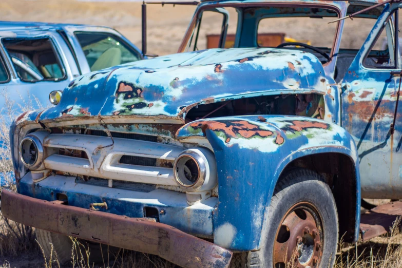 a rusted out old blue truck sitting in the grass