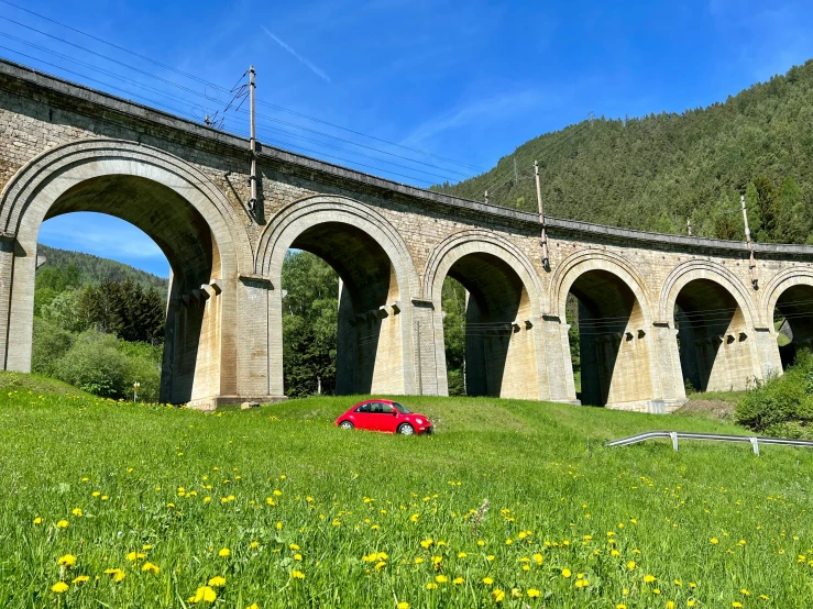 the red car is parked in front of an old stone bridge