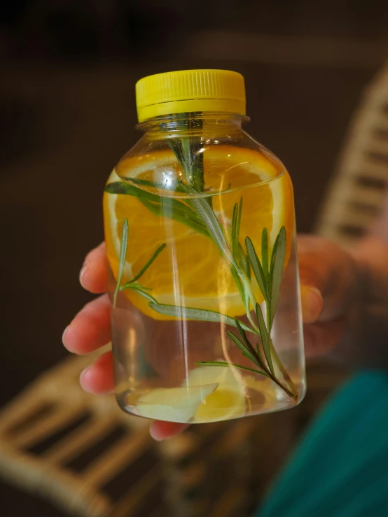 a hand holding a jar of liquid with an lemon and rosemary stem