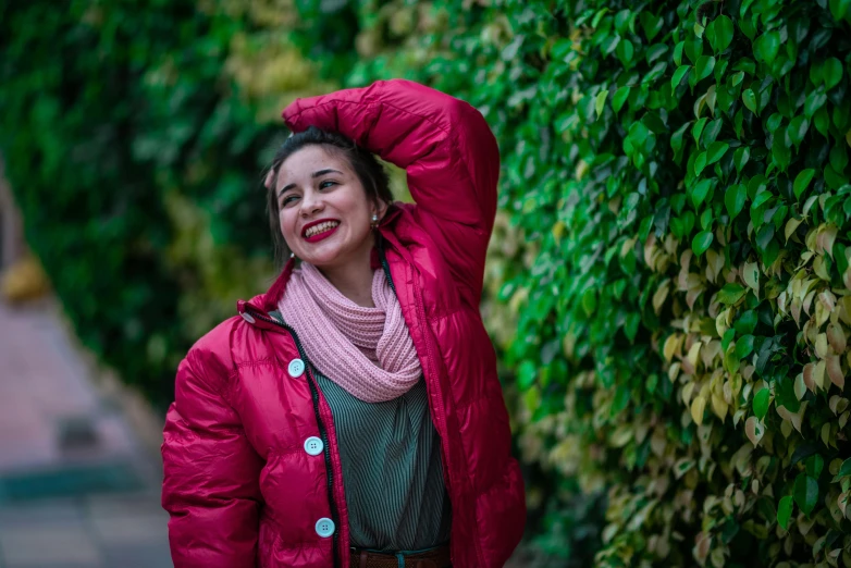 a woman wearing a coat smiling in front of bushes