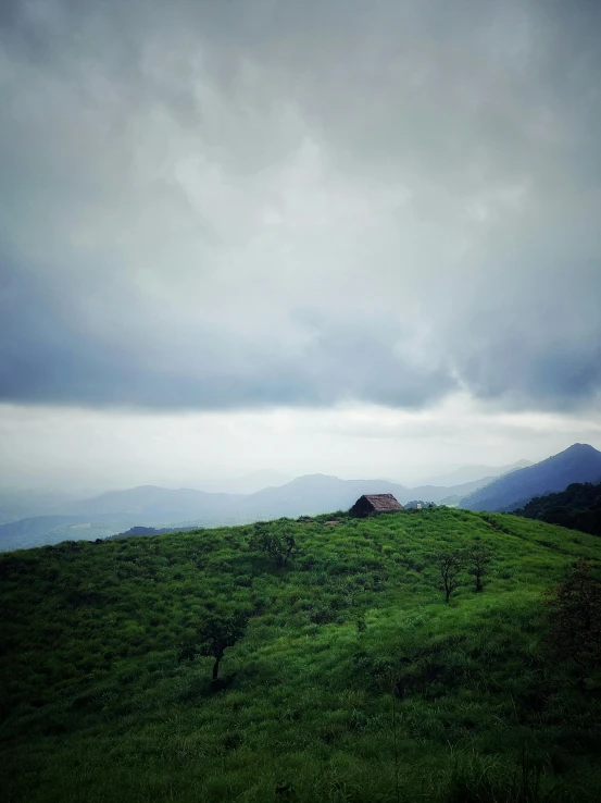 dark clouds hovering over a green landscape with a house