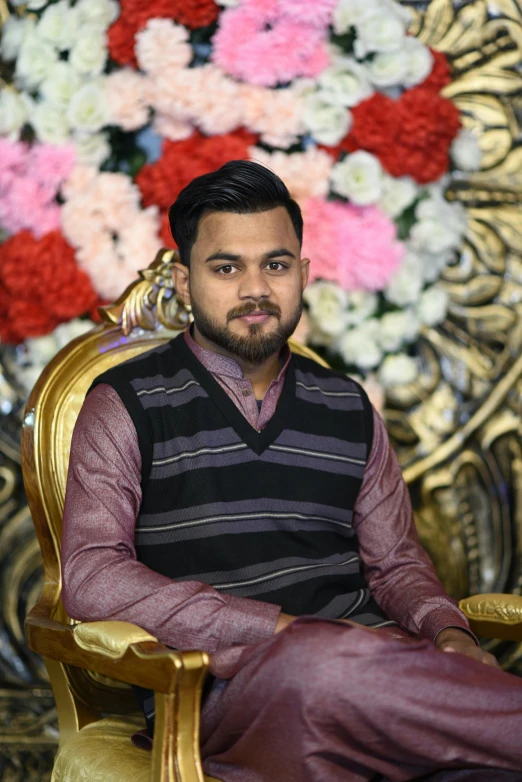 a young man sitting in a chair with flowers behind him