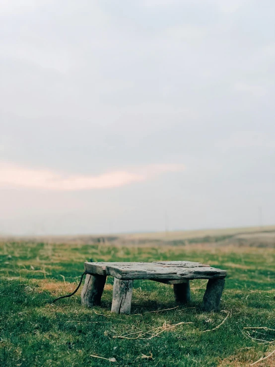 an empty bench sitting in the middle of a grass covered field