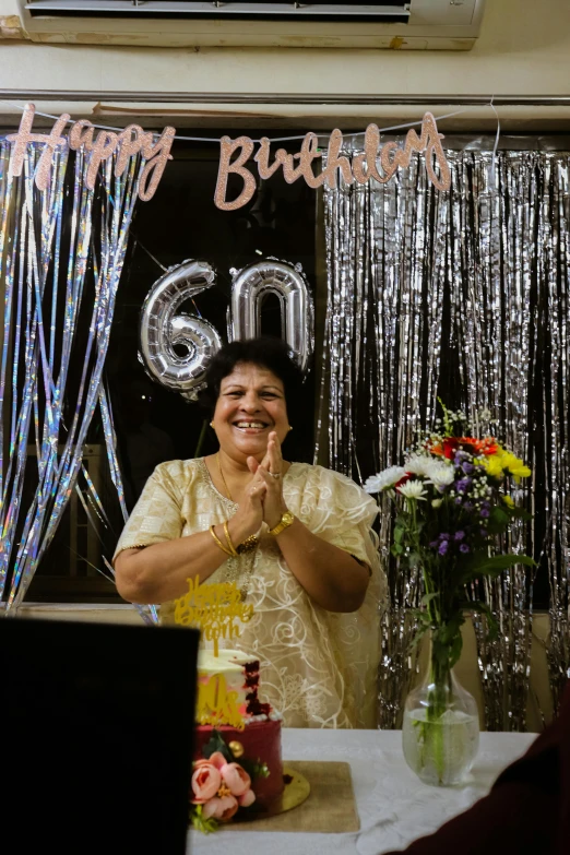 woman smiling while making a hush as she stands in front of the birthday banner