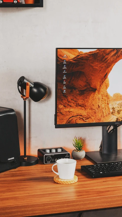 a desk with a computer monitor, keyboard, speakers and a cup