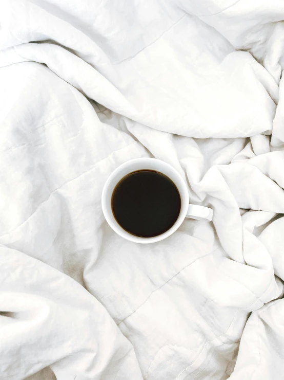 cup of coffee on top of a bed covered with white sheets