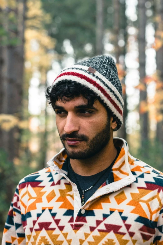 a young man wearing an colorful sweater and a fair weather hat is looking to his left