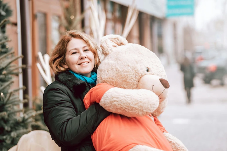 a woman in a coat is holding a giant teddy bear