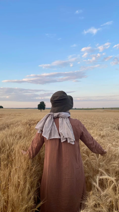 the back view of an old lady wearing a brown dress and hat in the middle of a wheat field